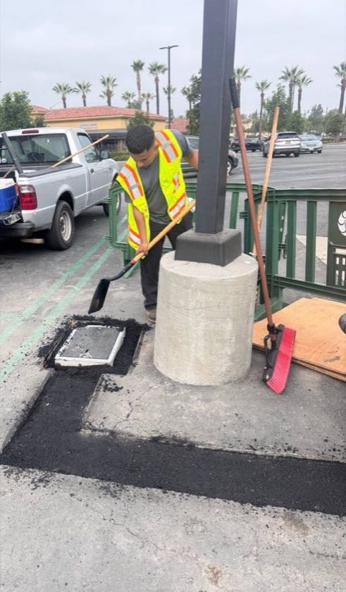 Ochoa Grading & Paving crew member placing asphalt in a trench in an Irvine parking lot